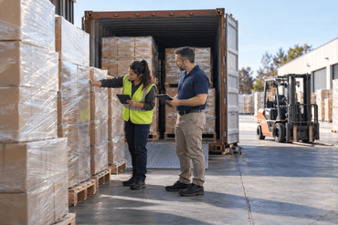 Warehouse team checking retail-stock pallets beside an open shipping container.